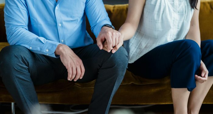 A couple sits together on a sofa holding hands, emphasizing togetherness and connection.
