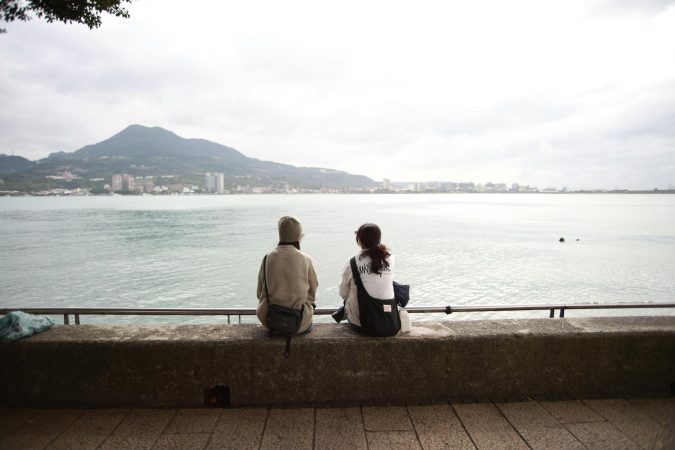 Two people sitting by the waterfront, gazing at distant mountains.
