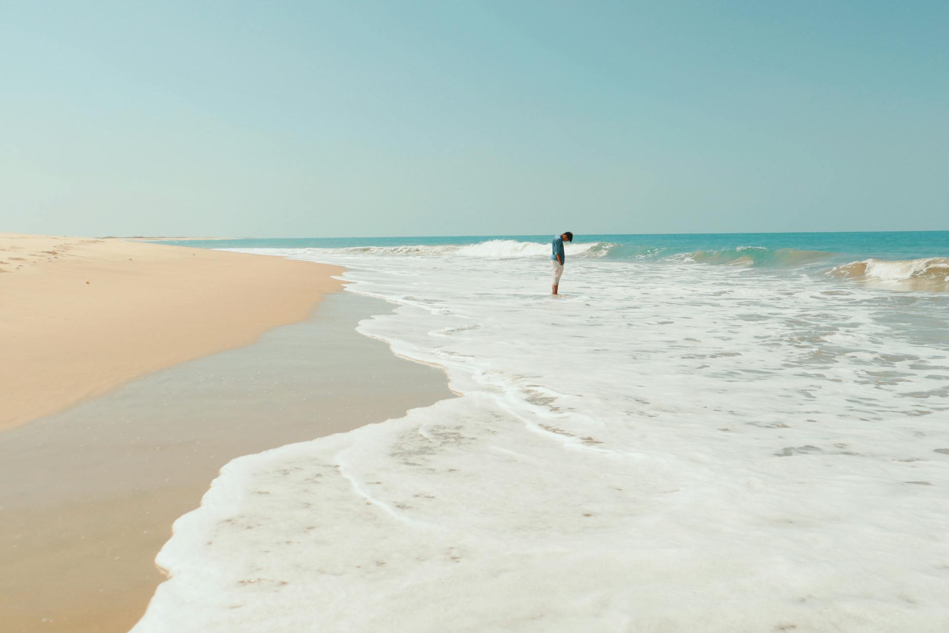 A lone person walks along a tranquil ocean shore, enjoying the gentle waves and peaceful atmosphere.