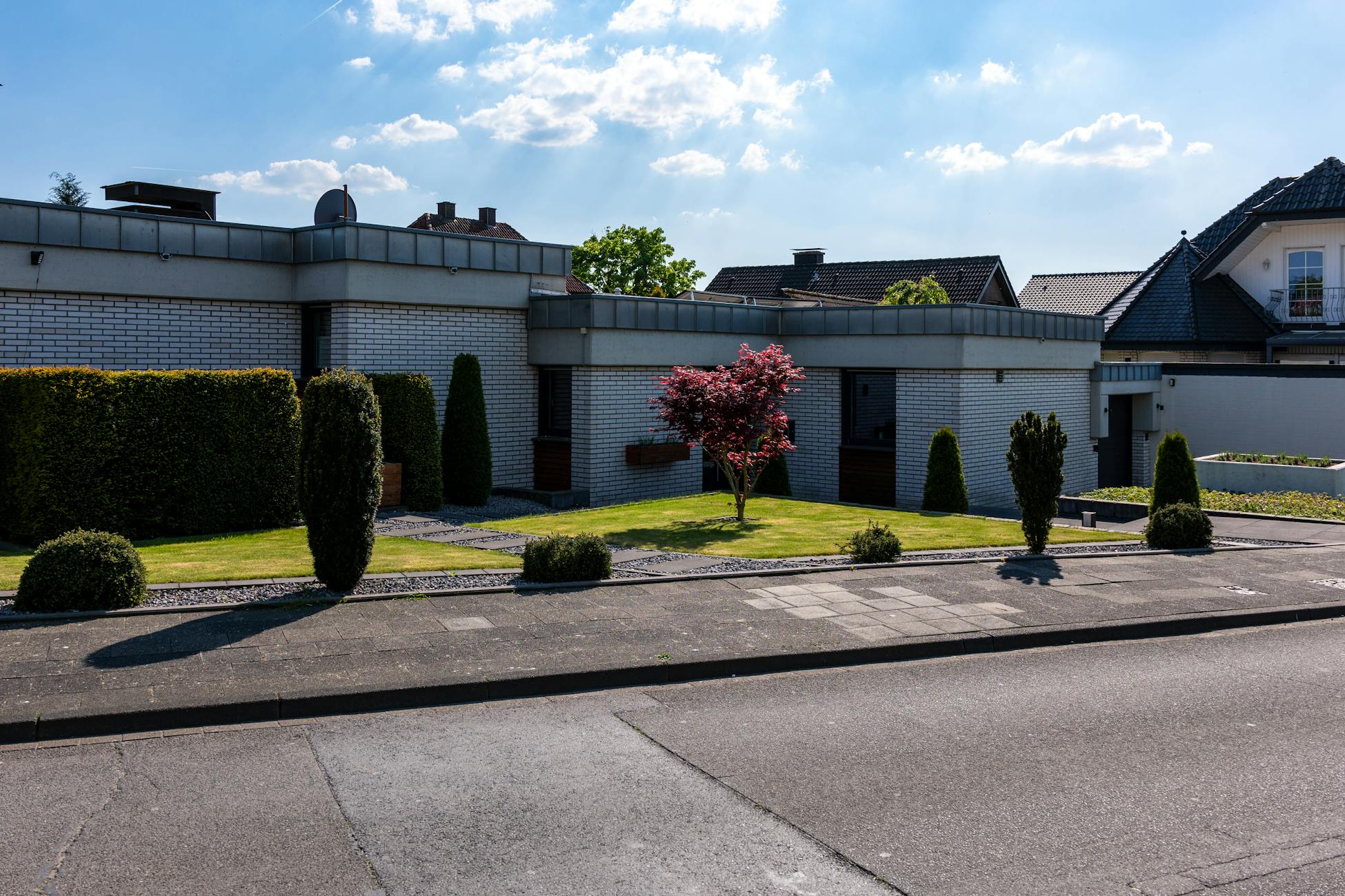 Contemporary suburban house with meticulous landscaping and modern architectural design on a sunny day.