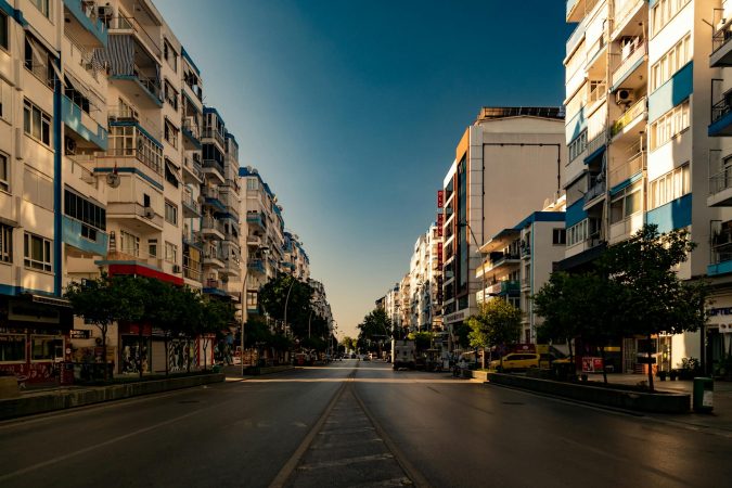 A deserted city street flanked by tall residential buildings in warm sunlight.