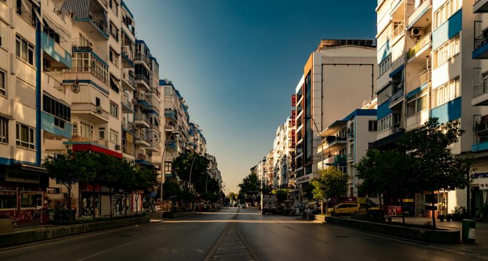 A deserted city street flanked by tall residential buildings in warm sunlight.