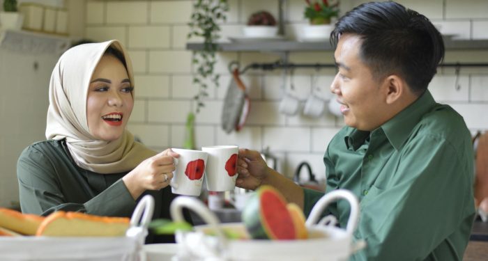 Smiling couple enjoying a warm drink while toasting in a cozy and stylish kitchen.